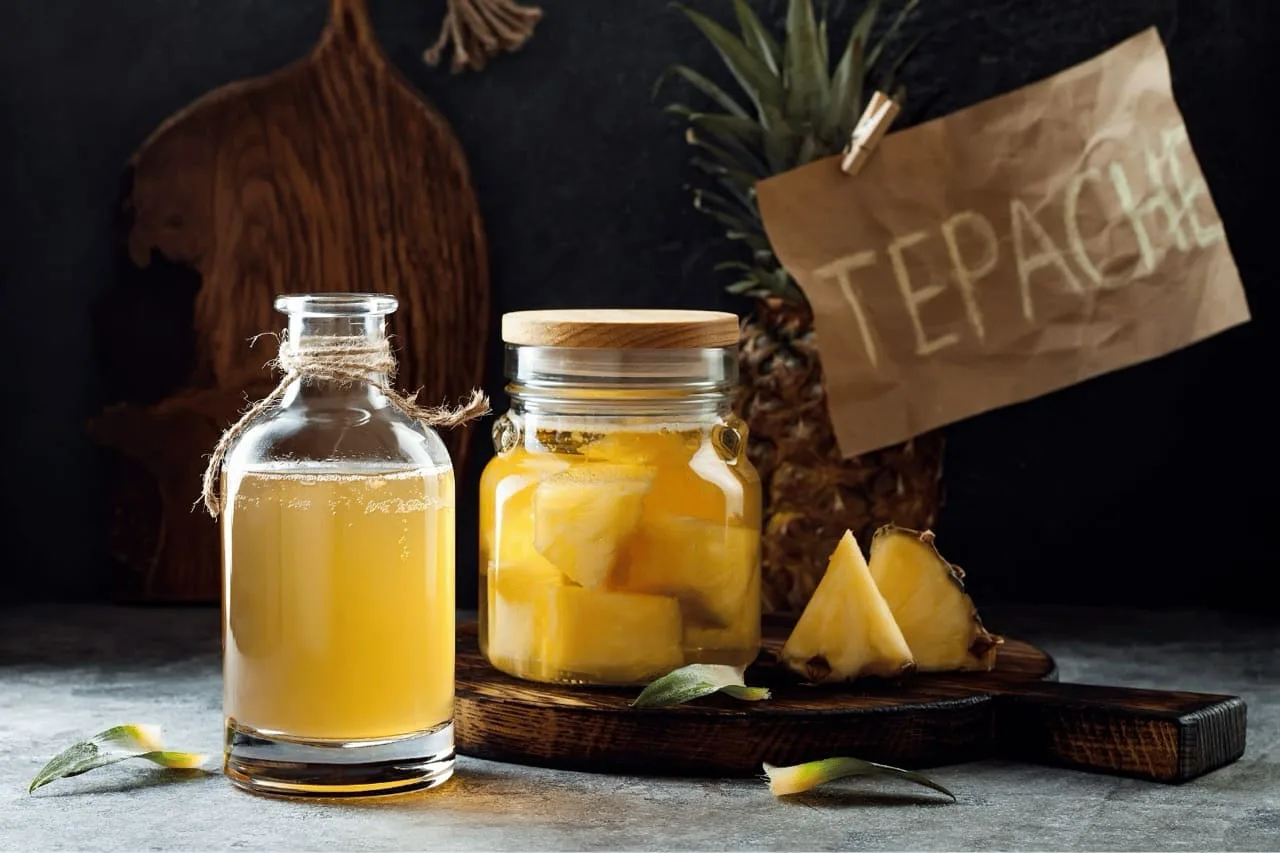 Tepache in una bottiglia di vetro e in un vaso di fermentazione con pezzi di ananas