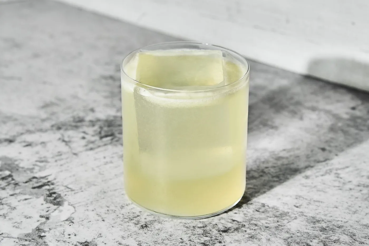 Tommy's Margarita in tumbler basso con grande cubo di ghiaccio su piano di marmo
