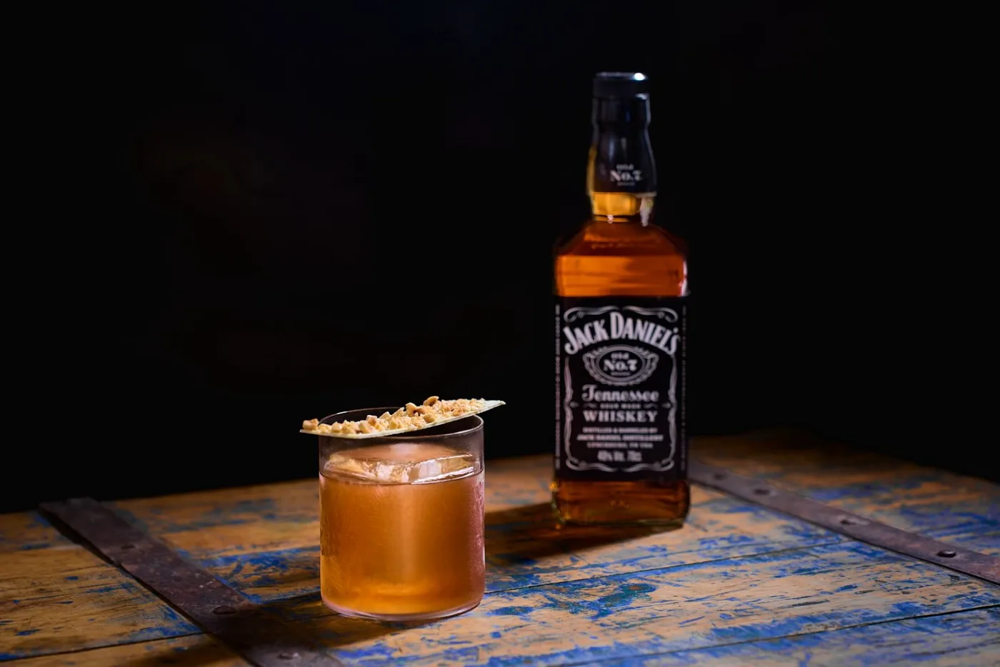 Twisted Nut: drink ambrato su chunk di ghiaccio decorato con cioccolato alla granella di nocciole, accanto alla bottiglia di Jack Daniel's Old No.7