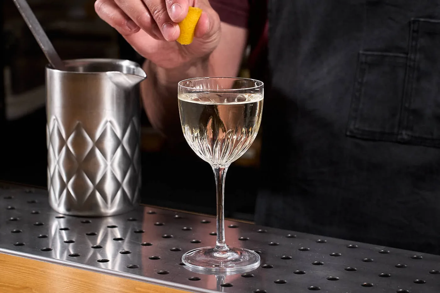Vesper Martini in coppetta mentre il bartender spreme un twist di limone sul drink, con il mixing glass alle spalle