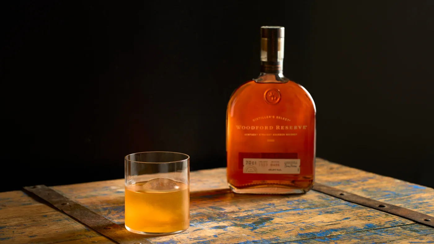 Wrong Way to Toronto: drink dorato su sfera di ghiaccio in tumbler basso accanto alla bottiglia di Woodford Reserve