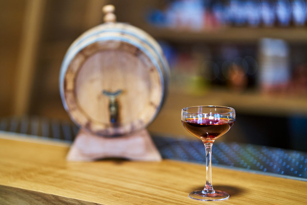 una foto di un Negroni perpetuo e di una botte da invecchiamento