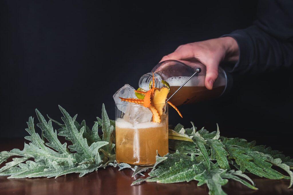 Alessandra versa il Cynar-INO nel bicchiere con ghiaccio decorato con scorze di agrumi