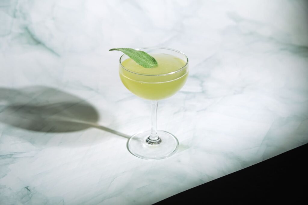 un cocktail in coppetta decorato con una foglia di salvia