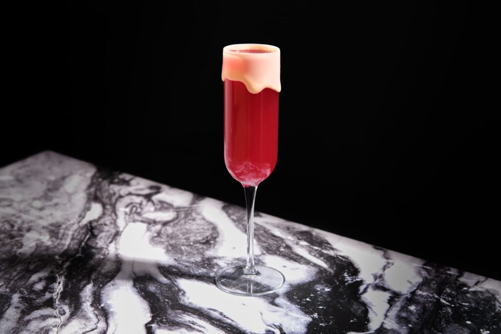 Un cocktail rosso alla barbabietola e fragola con una bordatura di cacao bianco fuso