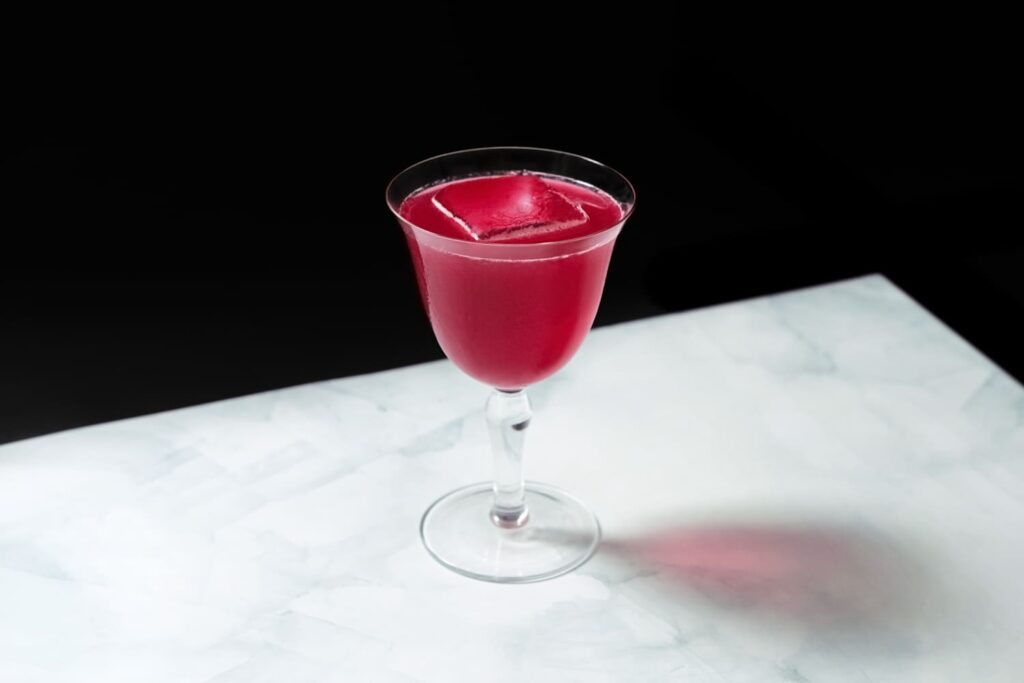 Un cocktail di colore rosso servito in coppetta a base tequila, barbabietola e mela