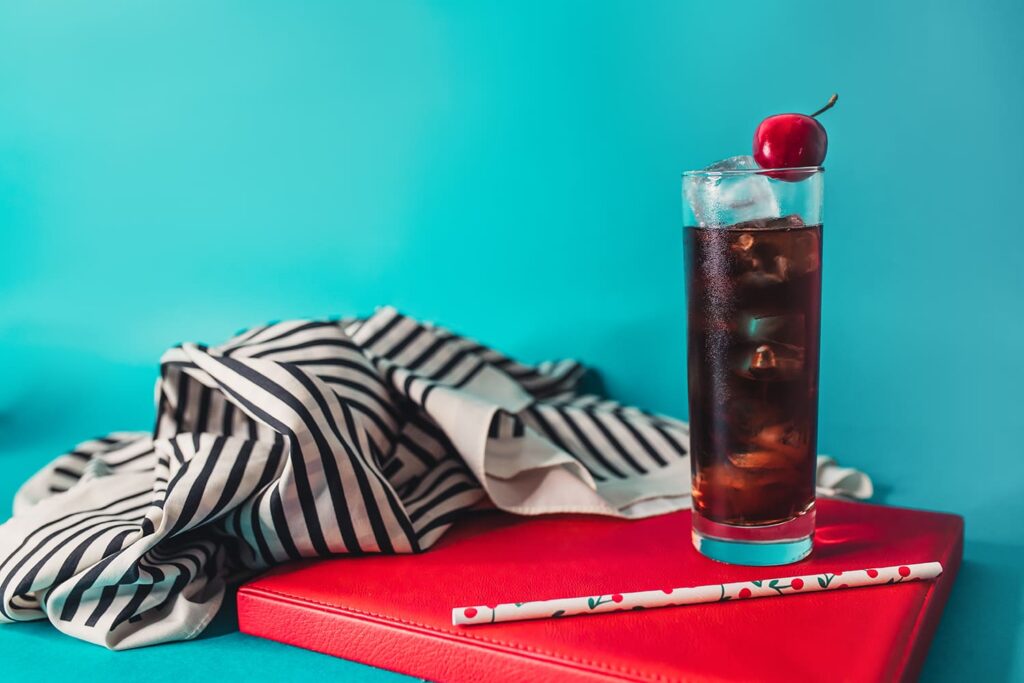 il drink Enjoy, a base rum e coca-cola alla ciliegia affumicata appoggiata su un libro rosso