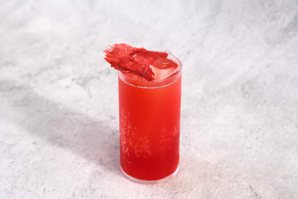 Un cocktail di colore rosso a base bitter e ciliegia, decorato con una patatina di ciliegie