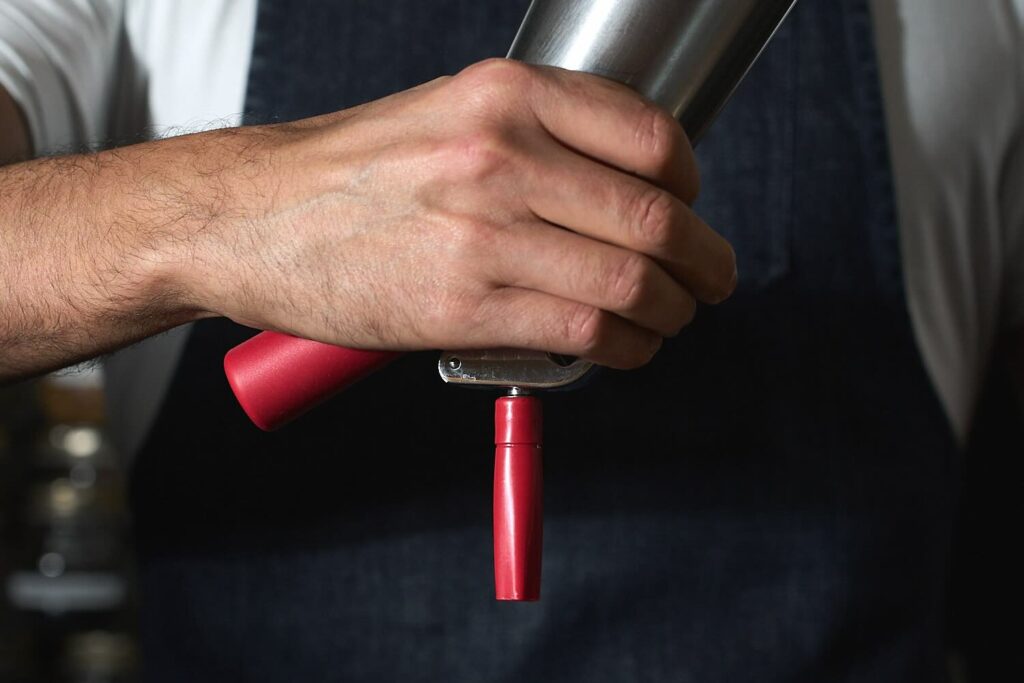 la mano di un barman che impugna un sifone pronto per erogare una foam