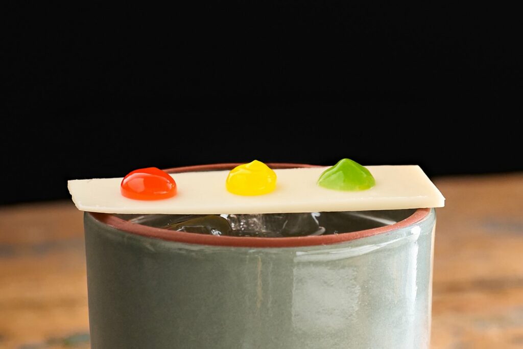Nella foto una striscia di cioccolato bianco posata su una mug in ceramica. Sul cioccolato ci sono 3 grosse gocce di gel fluido ai sapori di Fragola, Lime e Menta