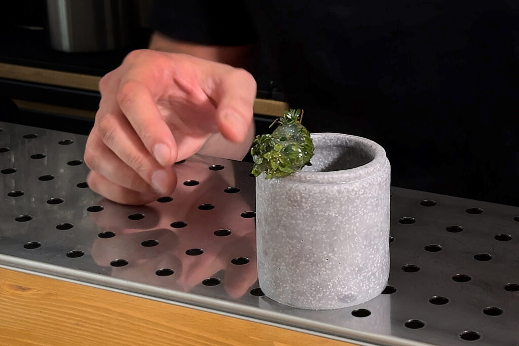 su un banco bar un vasetto in materiale ceramico grigio contenente il cocktail 