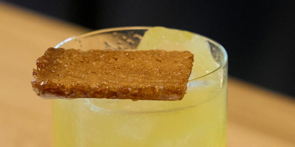 dettaglio della decorazione del cocktail guantanamera. La decorazione consiste in una sfoglia croccante simile ad un biscotto fatta con scarti di estrazione di ananas e glassa all'olio di cocco
