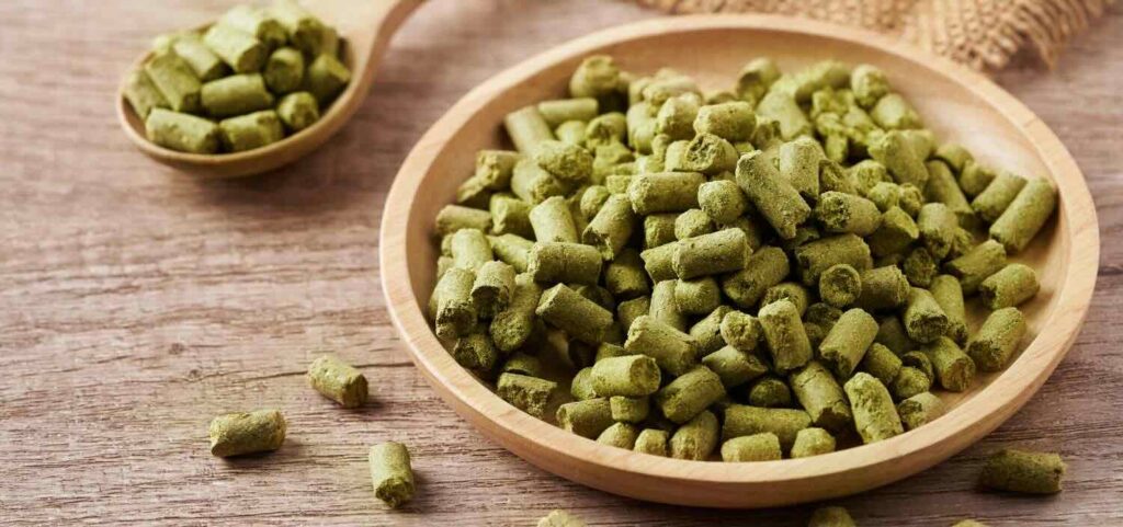 Su un tavolo di legno una ciotole e un cucchiaio in legno contenenti del Luppolo in pellet