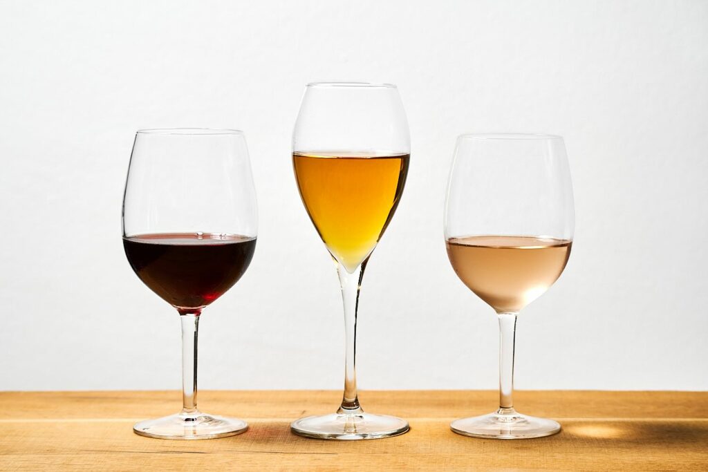 Su un tavolo in legno, 3 calici di vino con 3 vini diversi: uno rosso, uno bianco (tipo passito) e l'altro rosato