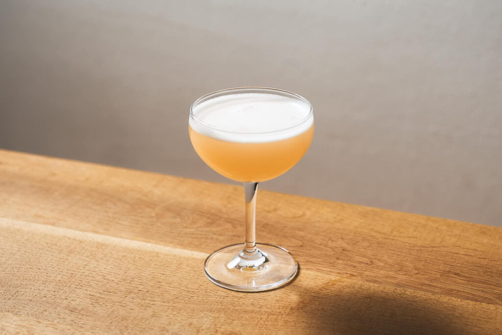Su un tavolo in legno, una coppetta da cocktail contenente il drink Mary Pickford. Iconico cocktail della miscelazione cubana preparato con rum cubano, succo fresco di ananas, granatina, Maraschi.