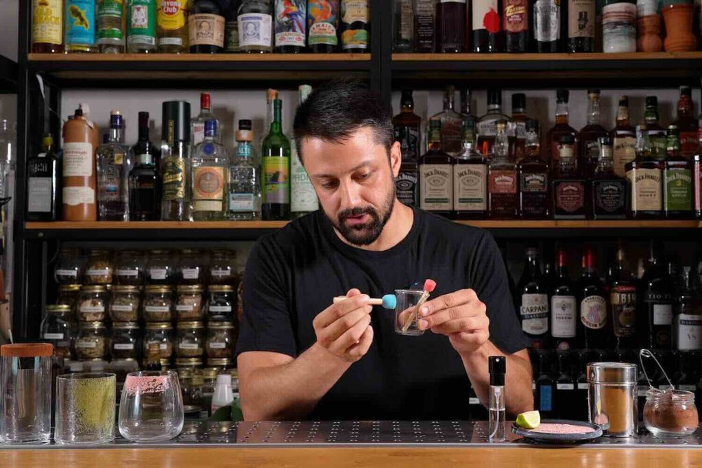Dietro un banco bar un bartender applica una decorazione ad un bicchiere con una piccola spugnetta decorativa