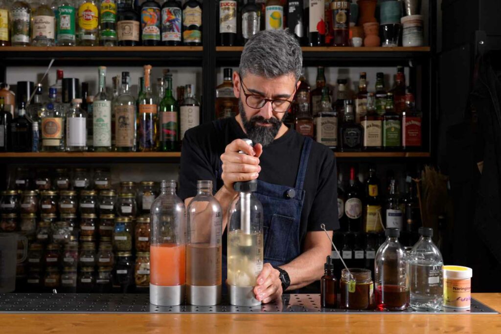 un bartender dietro al banco di un bar che sta utilizzando tre twist'n sparkle per gassare tre differenti sode al pompelmo realizzate home-made a partire da un succo di pompelmo privato della parte amaricante (grazie all'utilizzo dell'enzima naringinase) e poi riamaricate con 3 diversi ingredienti: un bitter, una tintura al carciofo, e miele di castagno