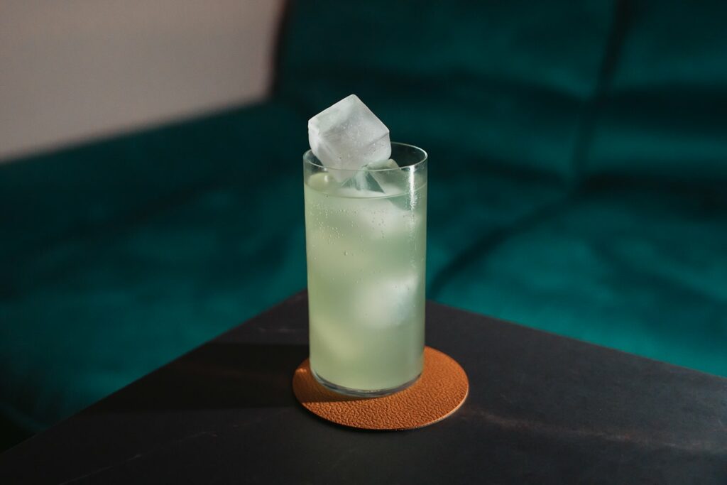 Su un tavolo un bicchiere da long drink contenente il cocktail "Quello Fico" preparato con Mezcal e soda alle pale di fico d'India.