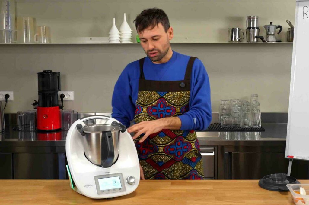 Giovanni Ceccarelli presenta un robot da cucina multifunzione, utile per le preparazioni home made. Il robot (bimby Vorwerk) è appoggiato su un piano in legno in un laboratorio.