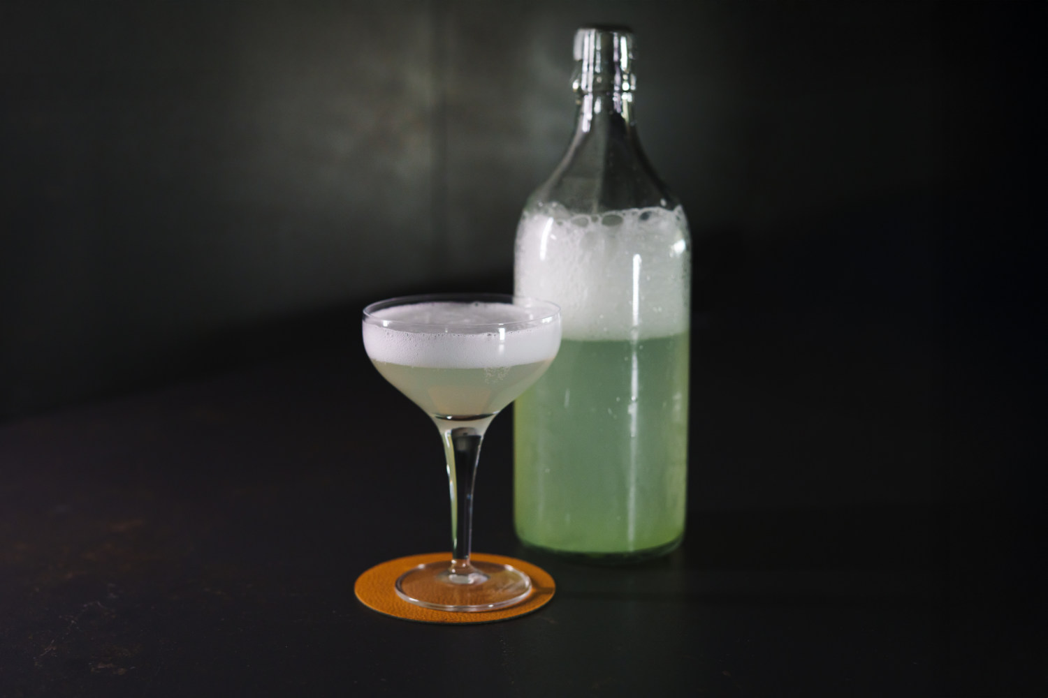 su un tavolo una bottiglia e un bicchiere da cocktail contenenti un fermentato di fiori di sambuco utilizzato come ingrediente nel cocktail 