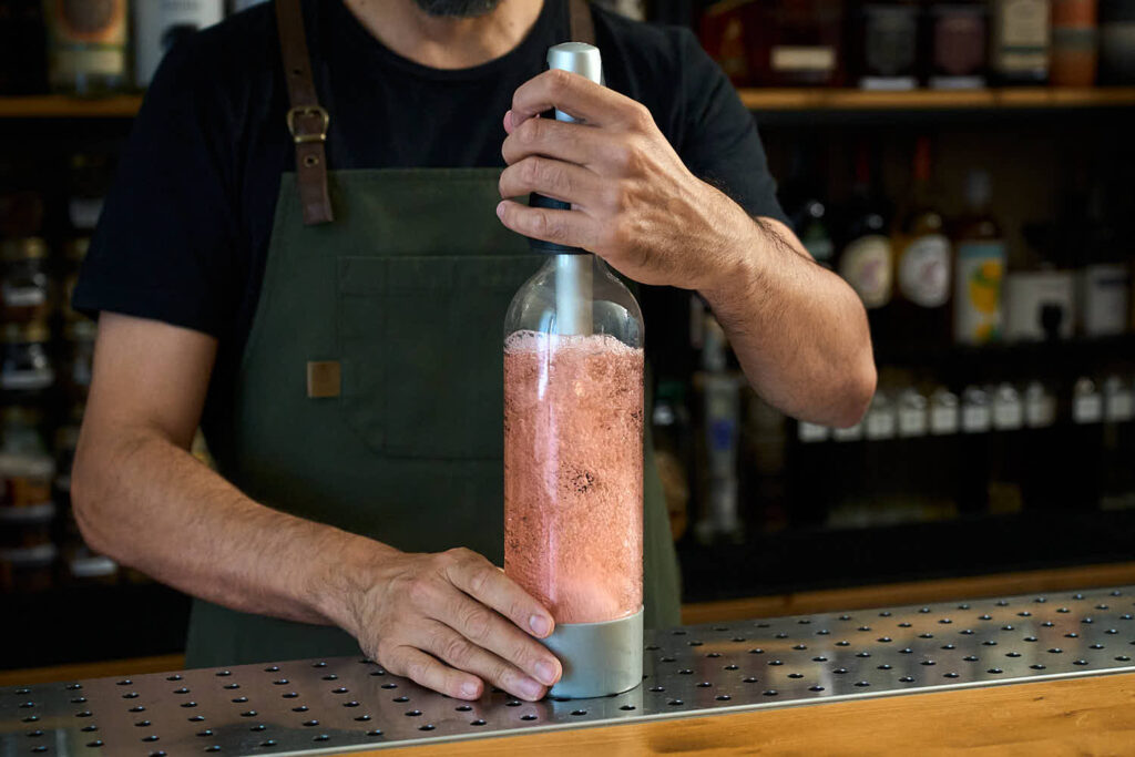 Su un banco bar un bartender sta gassando una soda ai pomodorini con un dispositivo Twist'n Sparkle.