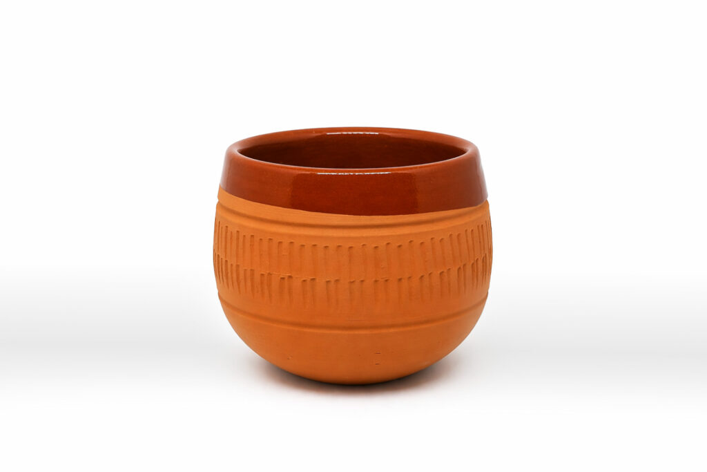 Una tazza in terracotta dalla forma arrotondata con delle decorazioni e la parte superiore smaltata.